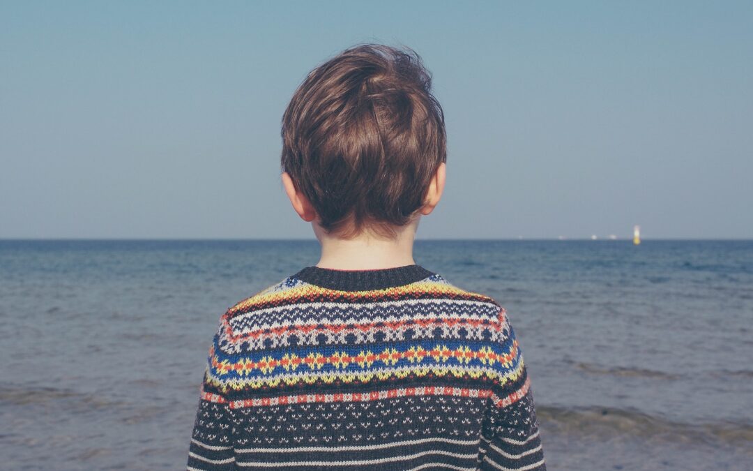 person wearing multicolored striped floral sweater facing the sea